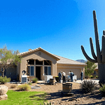 A serene Arizona landscape featuring a house with water damage, restoration technicians at work, drying equipment, bright blue sky, and desert plants.
