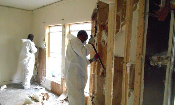 Fire damage restoration experts in protective gear meticulously cleaning and restoring a fire-damaged area.